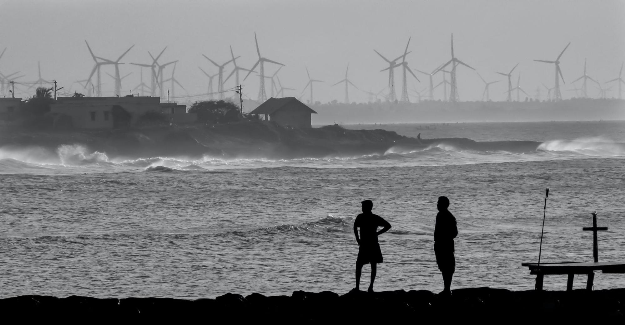Two men looking towards wind turbines in a coastal town